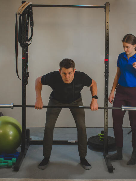 Erin is standing at an angle from a client, supervising a bent over row for therapeutic exercise.
