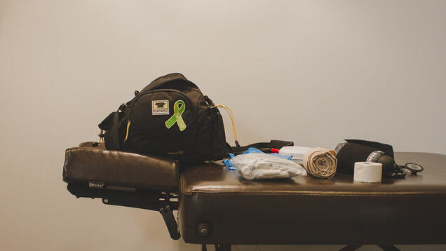 Erin's fanny pack is set up on her treatment table, displaying a Humboldt Broncos memorial pin for their Athletic Therapist Dayna Brons. Her emergency supplies and tape are laid out next to the fanny pack, ready to be used to help an athlete in need.